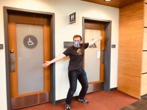 Nathan posing in a Stan State study abroad shirt before two closed bathrooms