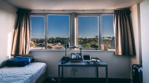 An empty dorm room with bed, window, and laptop